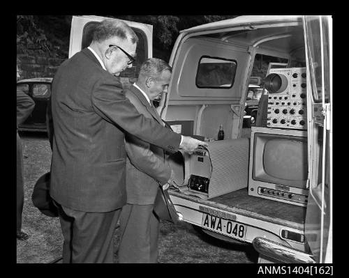 Photographic negative showing two men observing the live feed from an AWA underwater television camera