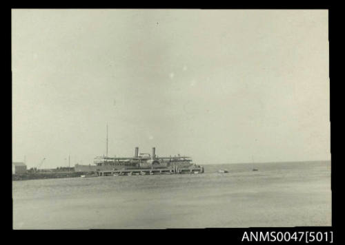 Distant view of a twin funnel paddle steamer at a wharf