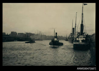 Mersey Towing Company Limited tug SS OTTER proceeding in port with wharves, vessels on either side