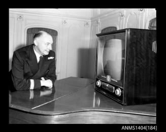 Photographic negative showing a man watching an AWA television on board the ship TAIPING