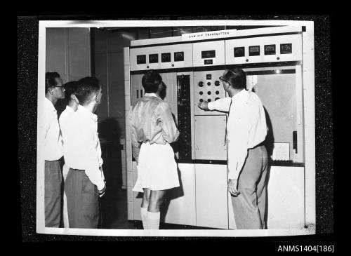 Photographic negative showing a group of men being shown an AWA brand transmitter on board a trade ship