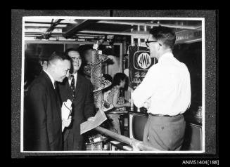 Photographic negative showing two men looking at an AWA company display on board a trade ship