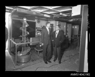 Photographic negative showing two men in front of an AWA company display on board a trade ship