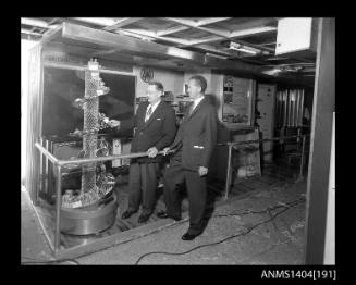 Photographic negative showing two men at an AWA company display on board a trade ship
