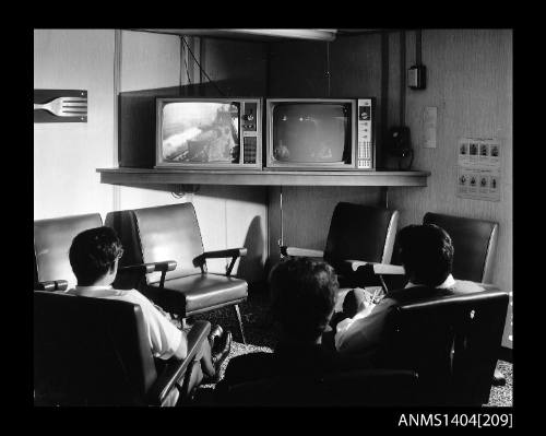 Photographic negative showing three men looking at two television sets on board the ship AUSTRALIAN TRADER