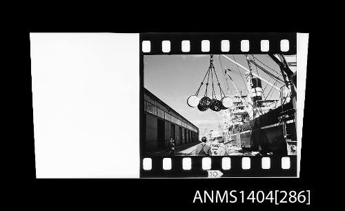 Photographic negative strip showing metal drums being loaded onto a cargo ship