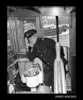 Photographic negative showing a Maritime Services Board officer demonstrating a telephone installed on the bridge of a small vessel