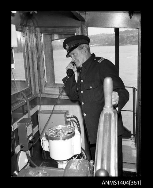 Photographic negative showing a Maritime Services Board officer demonstrating a telephone installed on the bridge of a small vessel