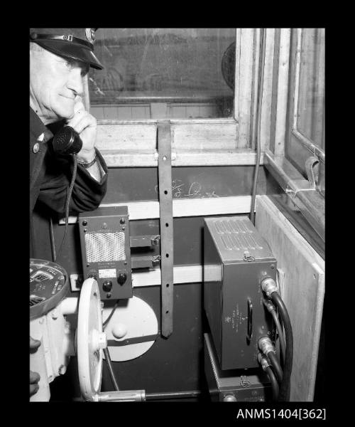 Photographic negative showing a Maritime Services Board officer demonstrating a telephone installed on the bridge of a small vessel