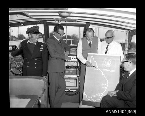 Photographic negative showing a group of men on board a boat with a poster of the AWA Australian radio network