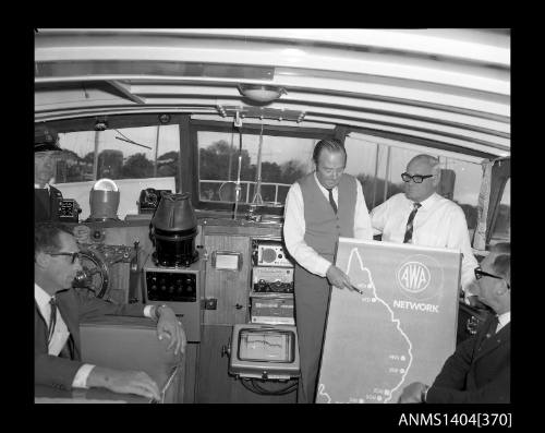 Photographic negative showing a group of men on board a boat with a poster of the AWA Australian radio network