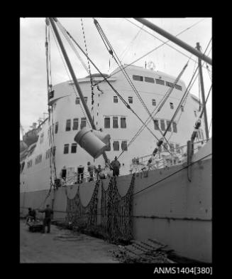 Photographic negative showing drums of paper being hoisted from a cargo vessel