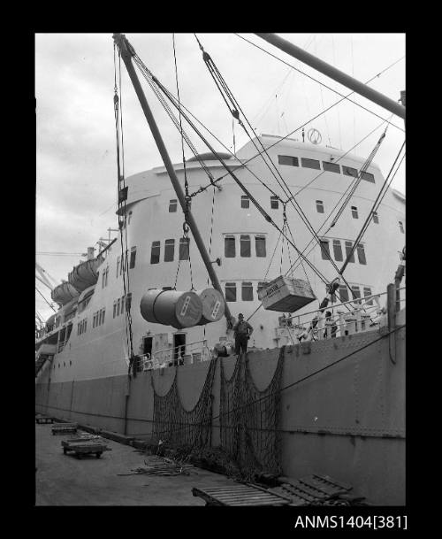 Photographic negative showing drums of paper being hoisted from a cargo vessel