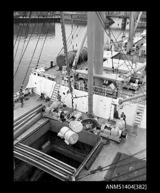 Photographic negative showing drums of paper being hoisted from the hold of a cargo vessel, with Glebe Island Bridge in background