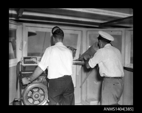 Photographic negative showing two men at the bridge of a boat operating various pieces of equipment