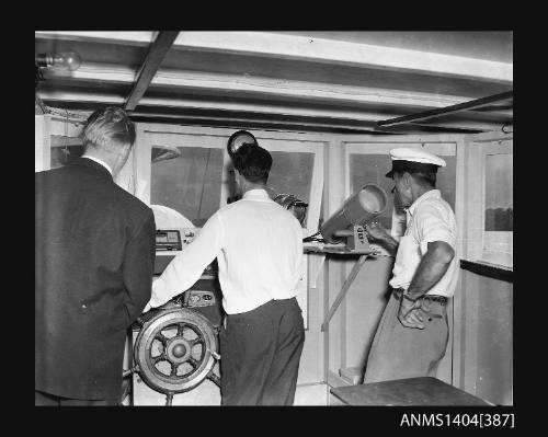 Photographic negative showing three men at the bridge of a boat operating various pieces of equipment