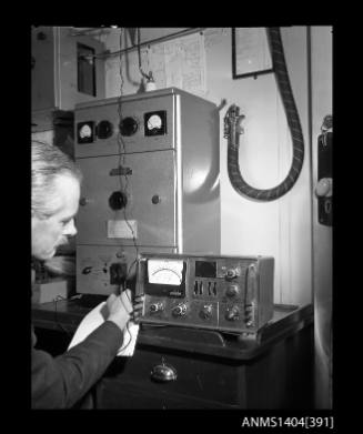Photographic negative showing a man testing an AWA radio communications unit on board a boat