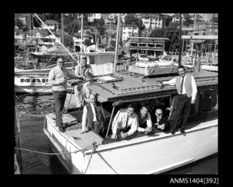 Photographic negative showing a group of nine men on a cruiser moored in front of the Cruising Yacht Club of Australia