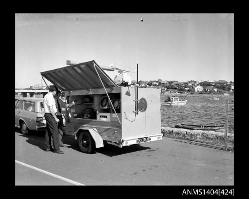 Photographic negative showing two men demonstrating navigational equipment contained in an AWA marine service trailer