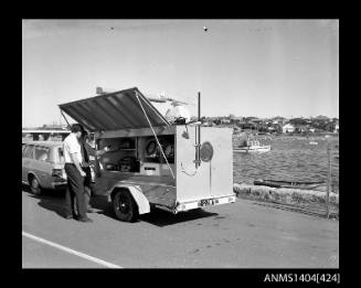 Photographic negative showing two men demonstrating navigational equipment contained in an AWA marine service trailer