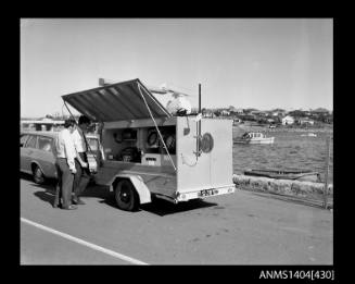 Photographic negative showing two men demonstrating navigational equipment contained in an AWA marine service trailer