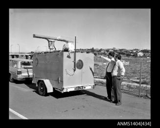 Photographic negative showing two men demonstrating navigational equipment contained in an AWA marine service trailer