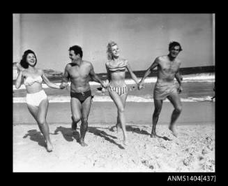 Men and two women in swimming costumes running on a beach