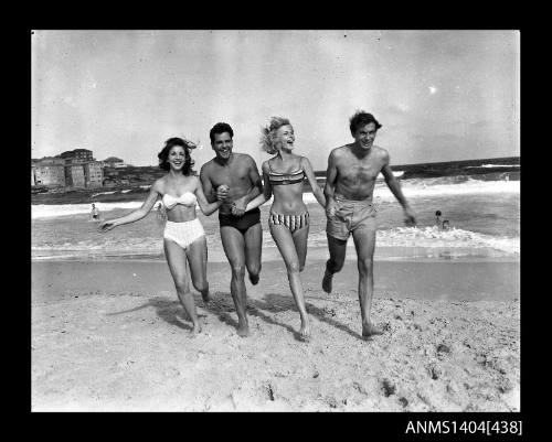 Photographic negative showing two men and two women in swimming costumes running on a beach