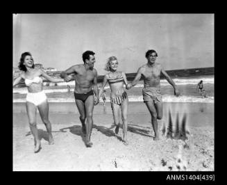 Photographic negative showing two men and two women in swimming costumes running on a beach