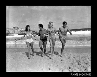 Photographic negative showing two men and two women in swimming costumes running on a beach