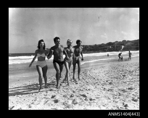 Photographic negative showing two men and two women in swimming costumes running on a beach