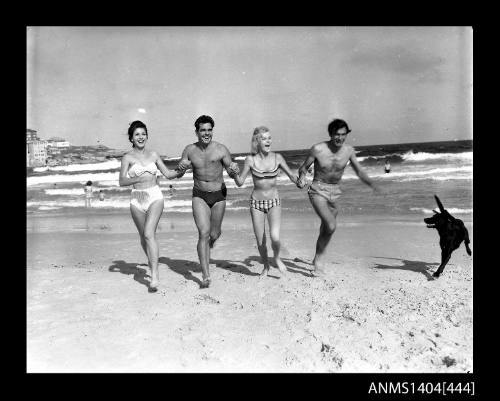 Photographic negative showing two men and two women in swimming costumes running on a beach