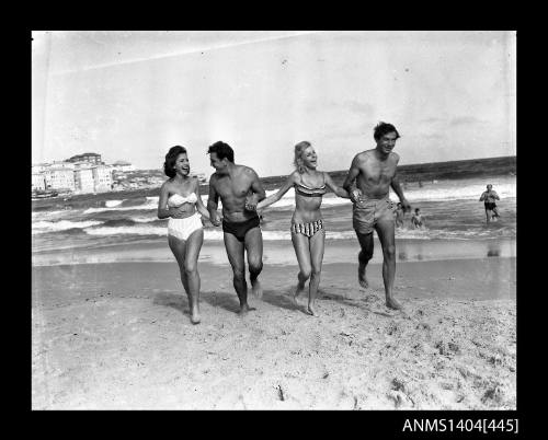 Photographic negative showing two men and two women in swimming costumes running on a beach