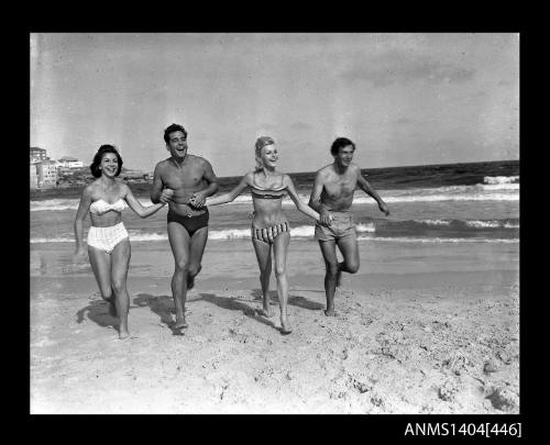 Photographic negative showing two men and two women in swimming costumes running on a beach