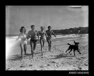 Two men and two women running on a beach with a dog