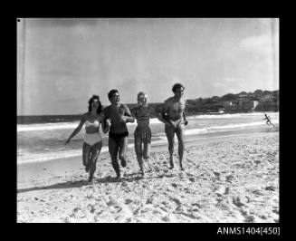 Photographic negative showing two men and two women in swimming costumes running on a beach