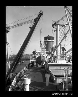Photographic negative showing an excavator being loaded onto a Blue Star Line ship with Glebe Island Bridge in background