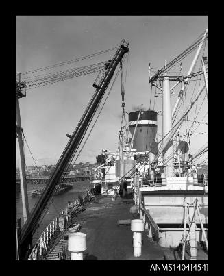 Photographic negative showing a wooden crate being loaded onto a Blue Star Line ship with Glebe Island Bridge in background