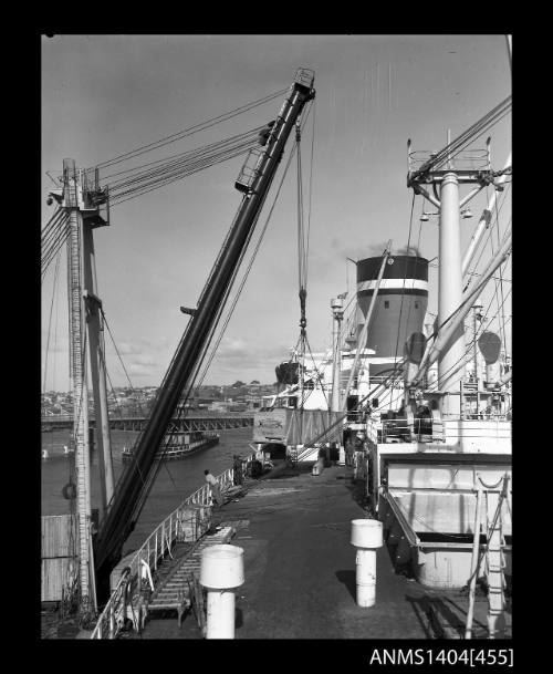 Photographic negative showing a wooden crate being loaded onto a Blue Star Line ship with Glebe Island Bridge in background