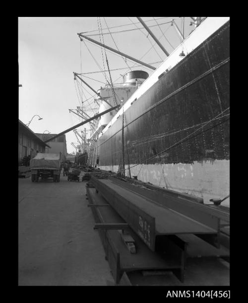 Photographic negative showing a cargo vessel at a wharf with steel I-beams about to be loaded