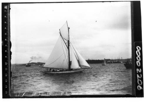 A gaff cutter sailing near Garden Island, Sydney Harbour, with four people visible onboard