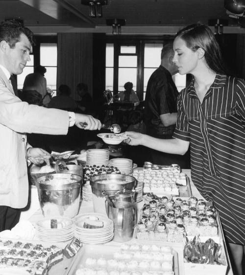 Photograph depicting a man serving ice cream to a woman from a buffet