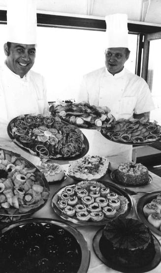 Photograph depicting two chefs with trays of food