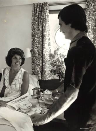 Photograph depicting a woman being served breakfast in her cabin