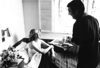 Photograph depicting a woman being served breakfast in her cabin