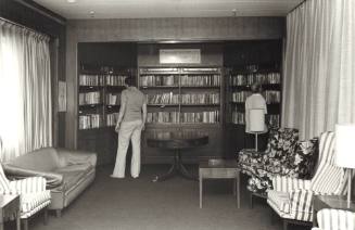 Photograph depicting two men looking at bookshelves at a ship's library