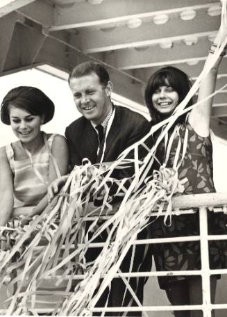 Photograph depicting three people at a ship's balcony throwing streamers