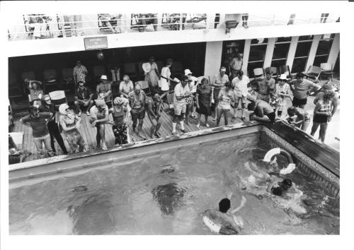 Photograph depicting passengers standing by the edge of the ship's pool