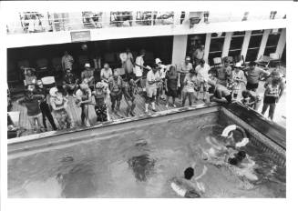 Photograph depicting passengers standing by the edge of the ship's pool