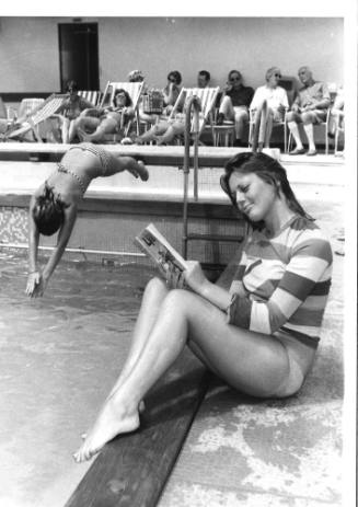 Photograph depicting a woman reading by the pool